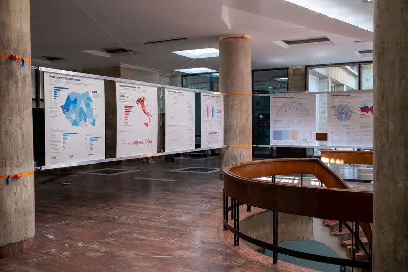 A line of hanging data panels crosses a pillared hall beside a round stairwell railing.