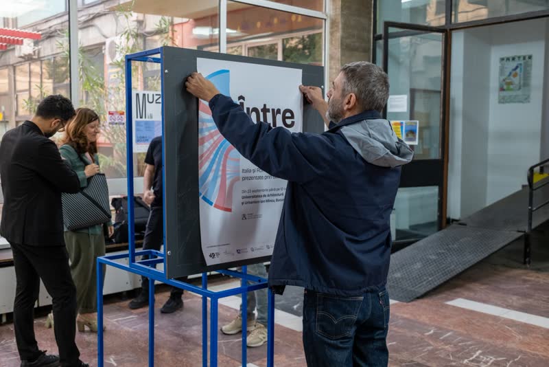 A man fixes the Între noi poster to a blue display stand at the entrance.