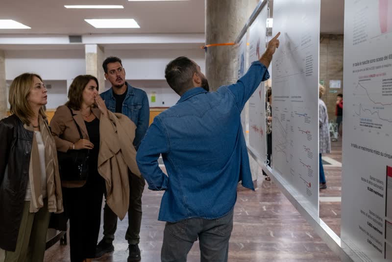 A man points at a chart while three visitors listen.